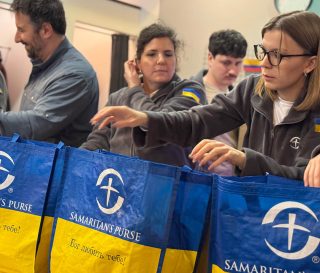 Samaritan's Purse staff pack emergency winter kits into bags labeled with 'God loves you' in Ukrainian