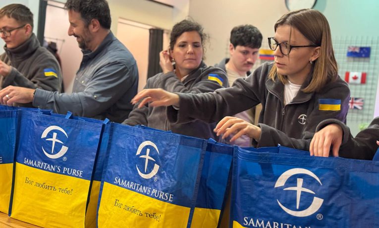 Samaritan's Purse staff pack emergency winter kits into bags labeled with 'God loves you' in Ukrainian