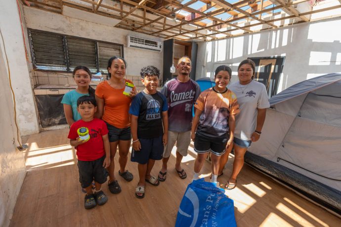 Crisotomo family stands in their roofless kitchen with tents set up for sleeping