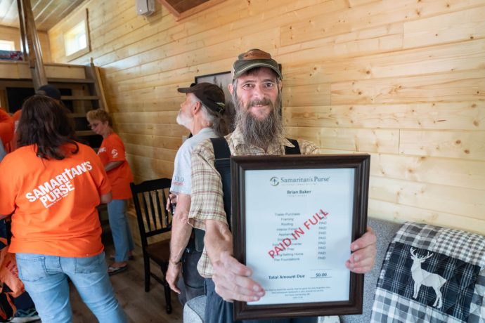 Brian shows off his "PAID IN FULL" invoice as volunteers linger in the background