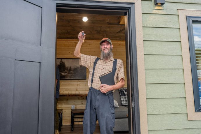 Brian stands in the doorway of his new home, showing off his new key and holding the Bible he received