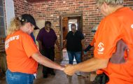 Orange-shirted volunteers pray with Louisiana homeowners