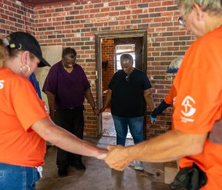 Orange-shirted volunteers pray with Louisiana homeowners