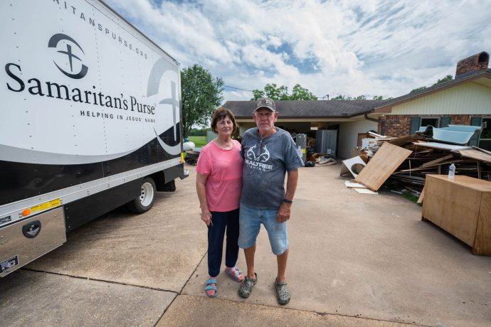 Linda and Wallace Morgan stand next to a Samaritan's Purse truck outside their flooded home