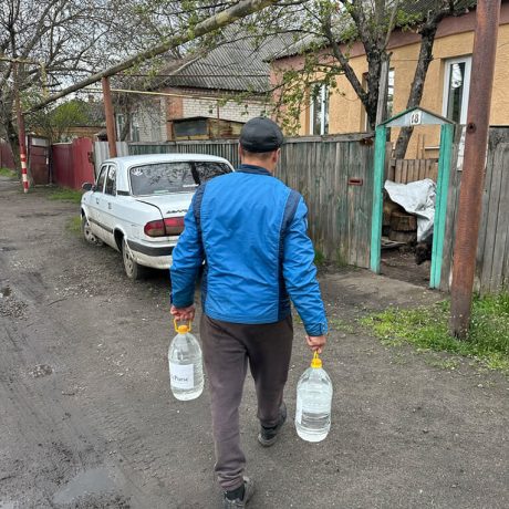 Michael approaches doorway to his home carrying two jugs of water