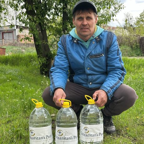 Michael crouching before three large water bottles from Samaritan's Purse