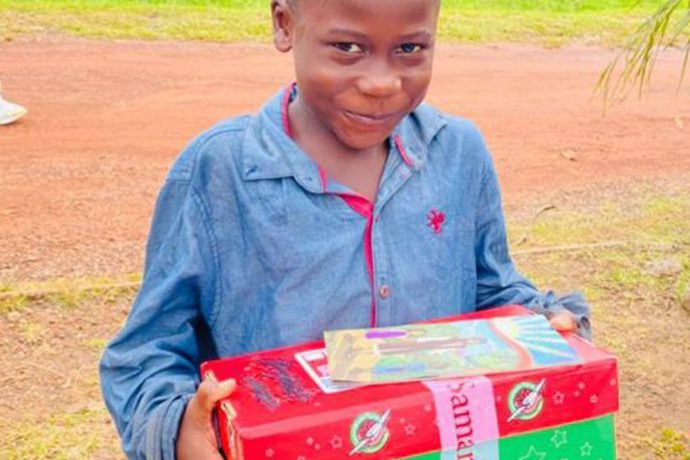 boy grins as he holds his shoebox gift and Gospel booklet
