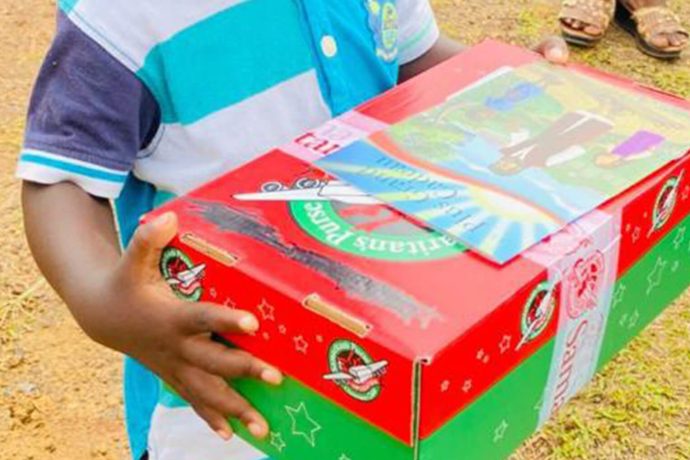 shoebox gift in the hands of a boy with a copy of a Gospel booklet on top