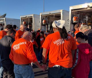 volunteers in orange T-shirts circle to pray in front of Disaster Relief Vehicles
