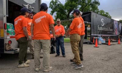 Volunteers in orange shirts stand in a circle near a Samaritan's Purse Disaster Relief Unit