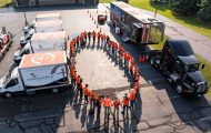Aerial view of orange-shirted volunteers circling to pray, surrounded by disaster relief vehicles