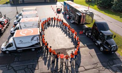 Aerial view of orange-shirted volunteers circling to pray, surrounded by disaster relief vehicles
