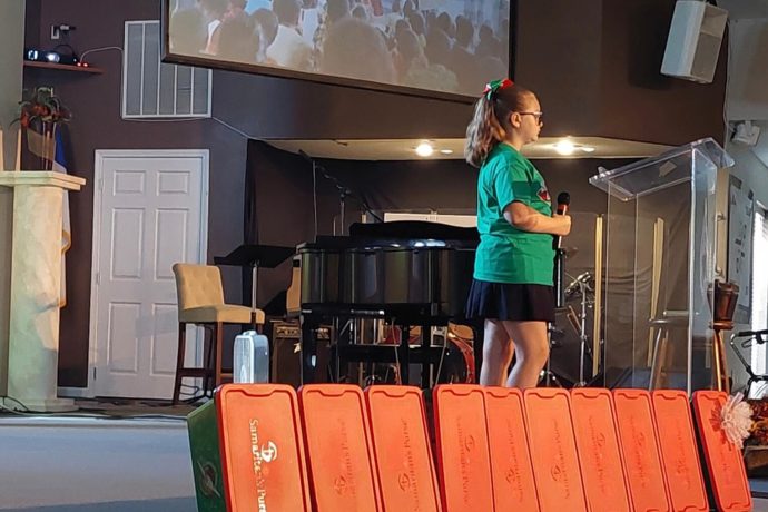 Abigail speaks at a church with a row of shoebox gifts on the stage