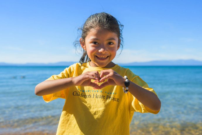 Dara holds her hands in a heart on the shore of a lake