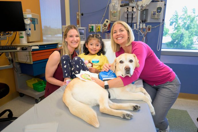 Hospital team including therapy dog pose with Dara at her hospital bed