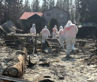 Voluntarios equipados con vestimenta de protección buscan entre las cenizas en Spokane.