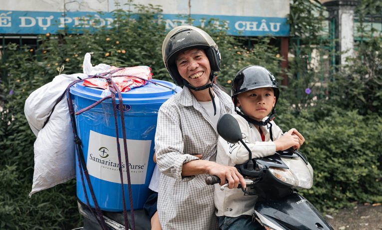 Man and child on motorbike with a can of Samaritan's Purse supplies on the back