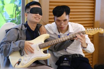 Phinh helps an attendee at Dining in the Dark learn how to play the guitar while blindfolded.